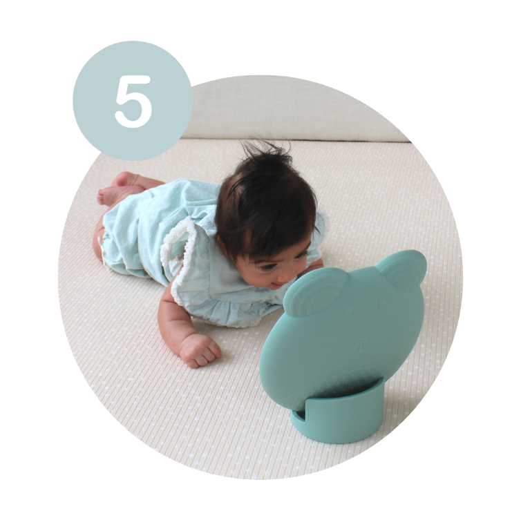 Baby looking at a green tummy time mirror whilst laying on a play mat